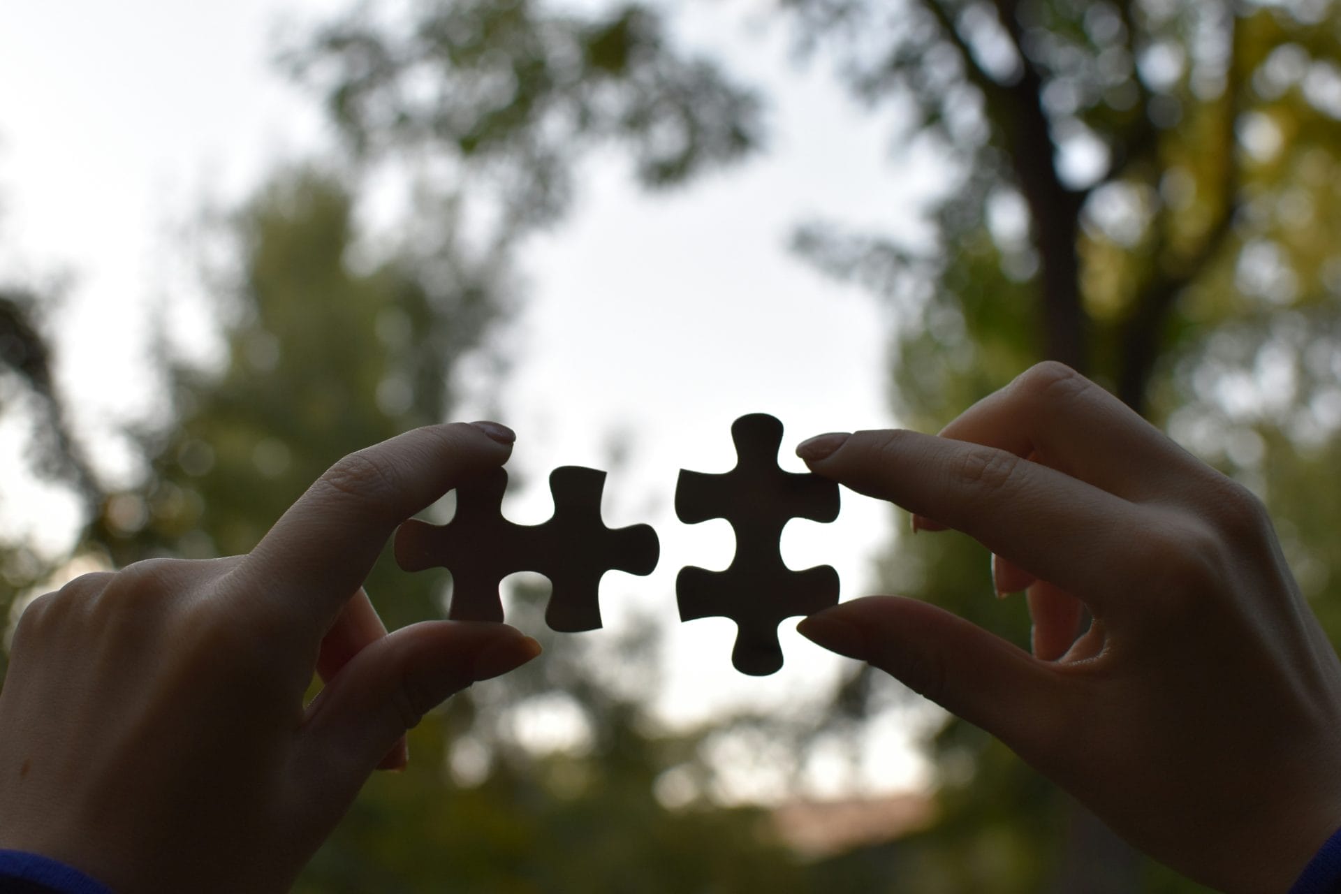 Hands holding two puzzle pieces outdoors, about to connect them.