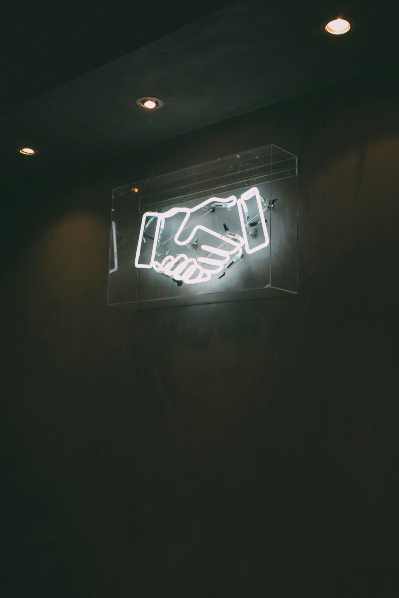 Neon sign of two hands shaking on a dark wall.
